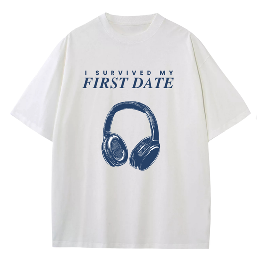 An pure white short-sleeve t-shirt with a navy blue graphic print that reads 'I SURVIVED MY FIRST DATE' above a large illustration of over-ear headphones.